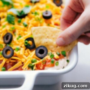 Ready-to-eat 7 layer bean dip being dipped into with a chip.