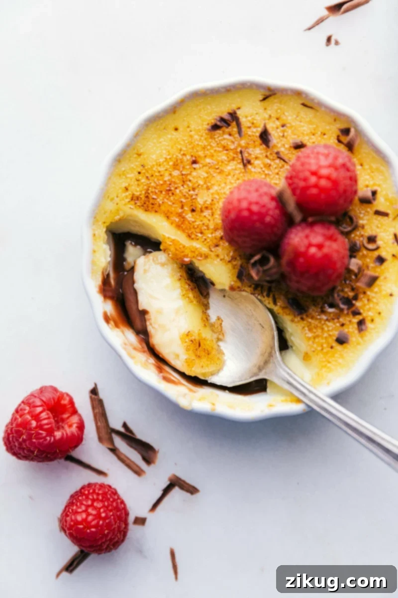 Tuxedo Crème Brûlée is a chocolatey twist on the traditional crème brûlée recipe. This dessert has a chocolate ganache bottom, creamy custard filling, and a caramelized sugar topping. Top these brulée with fresh berries and chocolate curls for a delicious show-stopping dessert. Recipe via ChelseasMessyApron.com #cremebrulee #tuxedo #ganache #French #dessert #elegant Image of a spoonful being taken out of these Tuxedo crèmes brûlée.