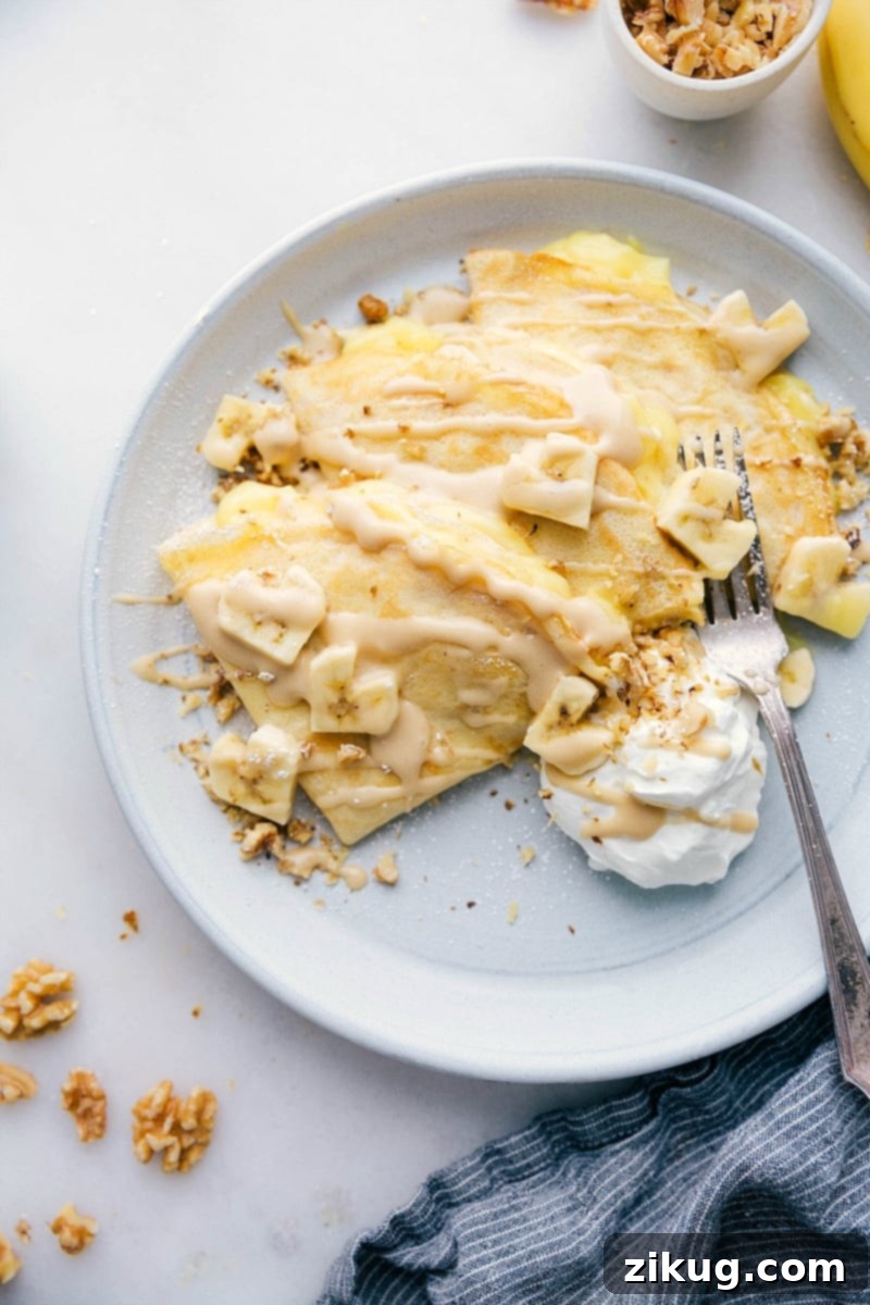 This simple crepe recipe is filled with an easy custard filling, plenty of bananas, and chopped walnuts. Banana Crepes are easy to make -- the actual crepes and custard can be made ahead of time so when you're ready to serve, everything comes together in a flash. Recipe via ChelseasMessyApron.com #crepes #bananas #custart #walnuts #breakfast Overhead photo of a plate of Banana Crepes. Bananas are cut into heart shapes! A perfect romantic breakfast.