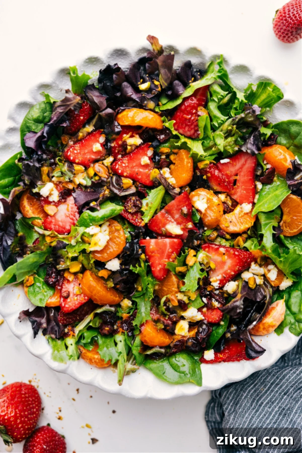A vibrant Strawberry Salad mixed with fresh greens, clementines, cranberries, pistachios, and creamy goat cheese, drizzled with citrus dressing, ready to be enjoyed.