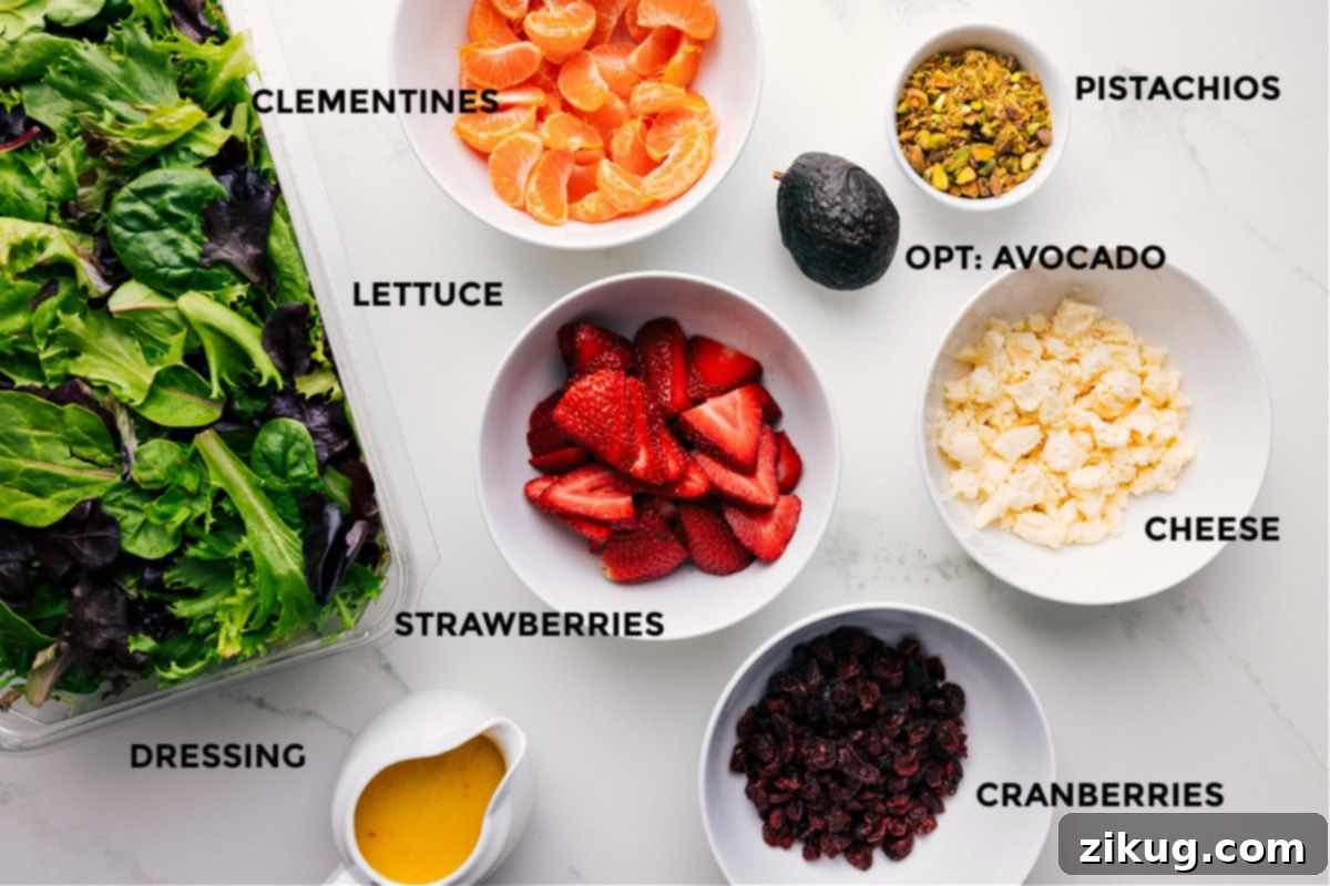All the fresh ingredients for Strawberry Salad are prepped and laid out, including vibrant strawberries, peeled clementines, mixed greens, pistachios, dried cranberries, creamy goat cheese, and a jar of homemade citrus dressing.