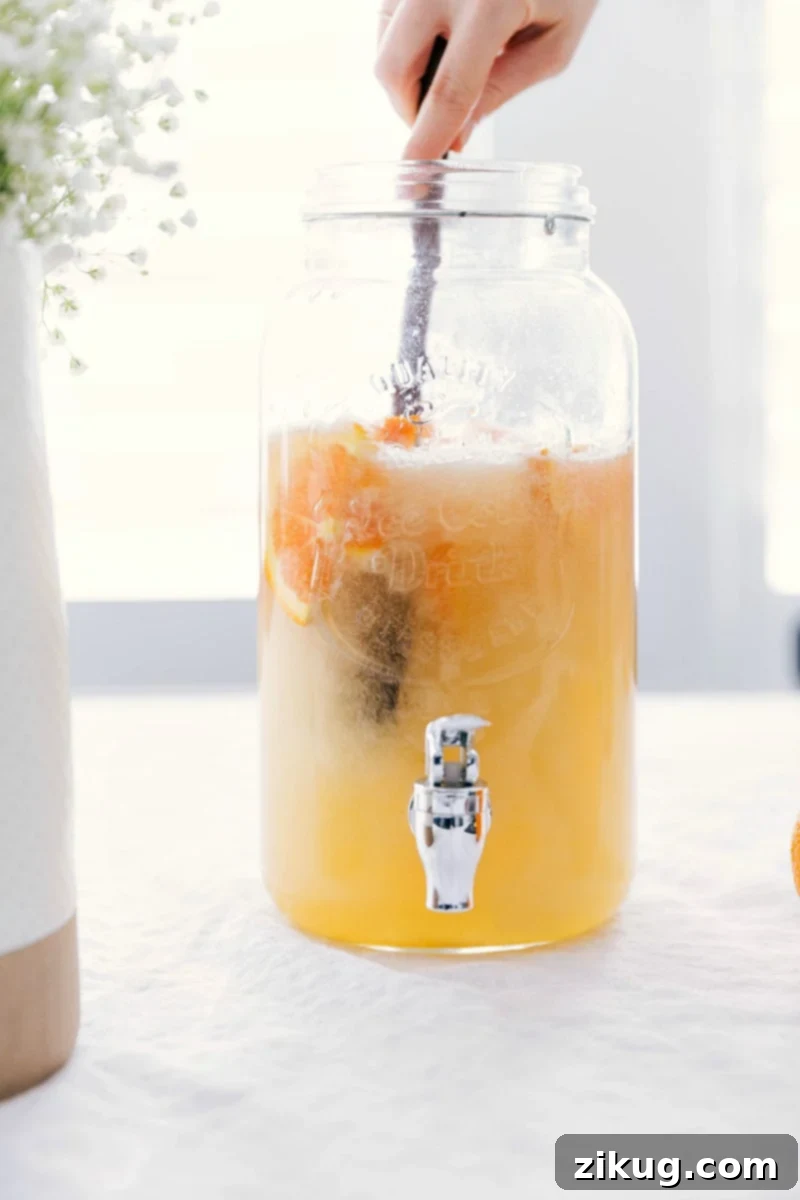 A large, clear beverage dispenser holds the refreshing drink, stirred to perfection, with fruit slices and berries visible, ready to be served.