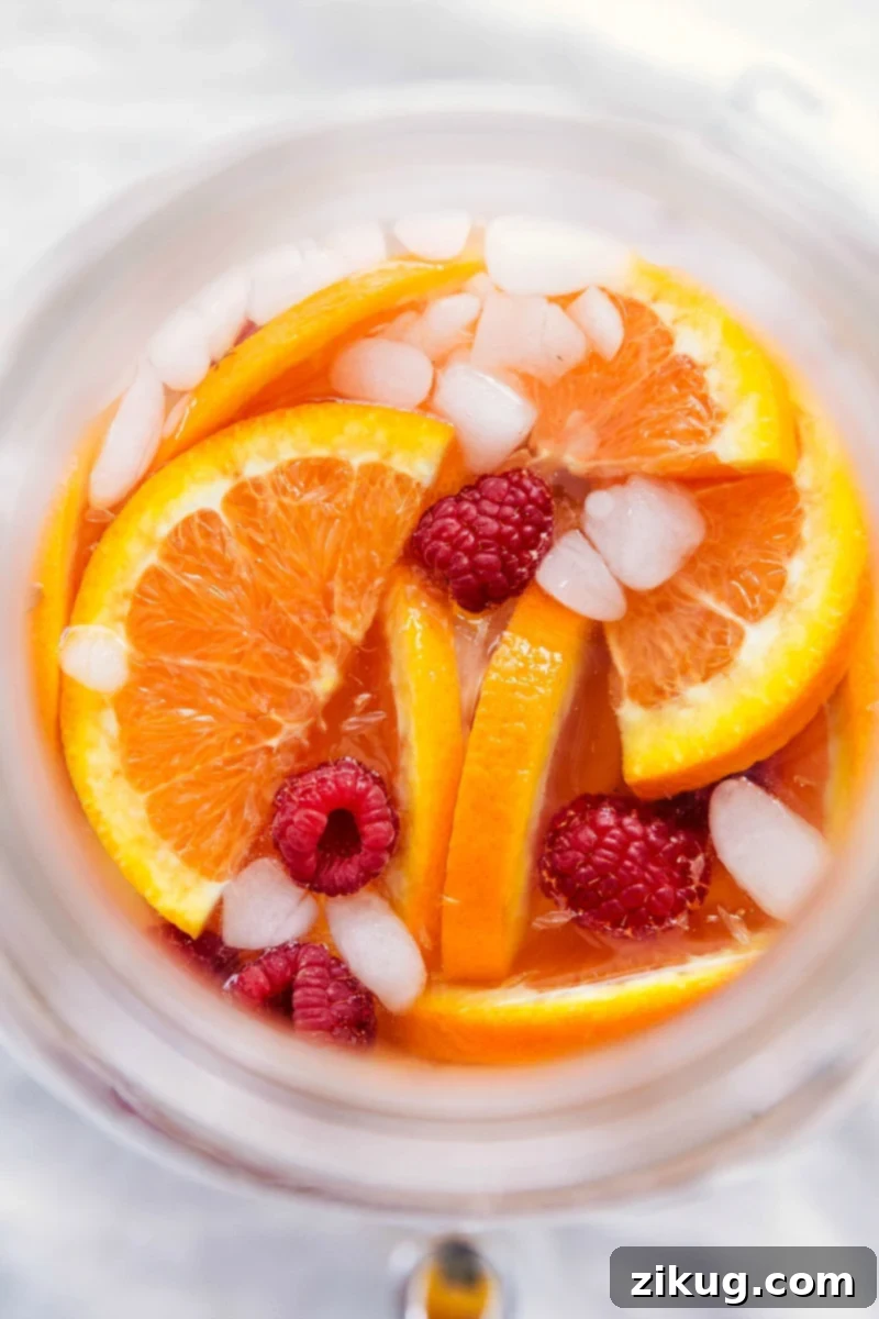 A close-up shot of a glass filled with the easy white grape punch, adorned with fresh orange slices, raspberries, and ice, ready for enjoyment.