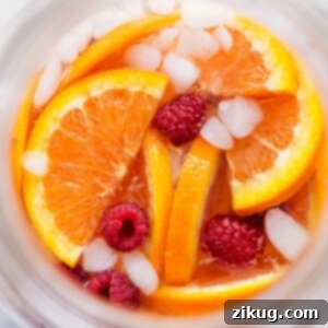A glass of punch with oranges, raspberries, and ice, ready to be enjoyed.