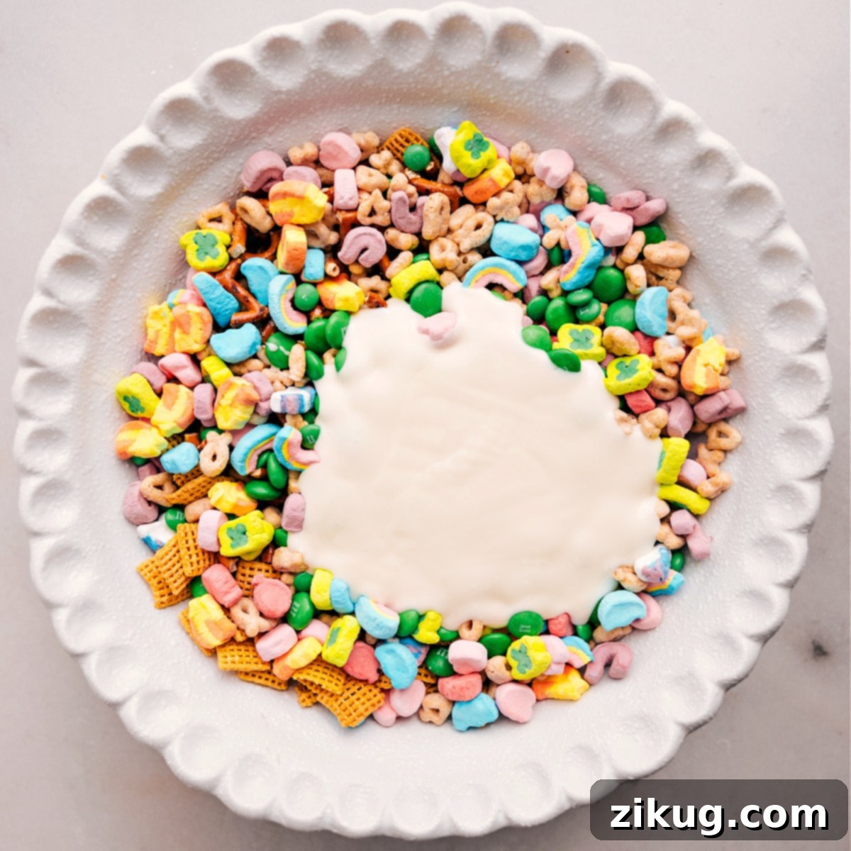 The Perfect St. Patricks Day Recipe: Leprechaun Bait Melted white chocolate is being generously poured over the mixed dry ingredients of Leprechaun Bait, ready for a thorough mix.