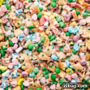 A top-down shot of a bowl filled with finished Leprechaun Bait, showing the white chocolate coating, Lucky Charms, pretzels, and green M&Ms.