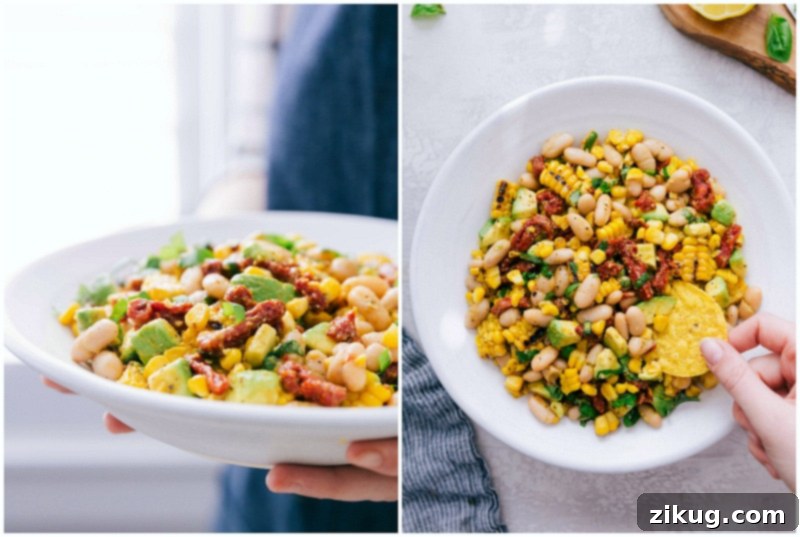 This incredible White Bean Salsa with creamy avocado, crisp corn, savory sun-dried tomatoes, fresh lemon, and sweet basil is our absolute favorite! It's perfect over grilled Pesto Chicken, making for an unforgettable meal. Recipe via Chelseasmessyapron. #healthy #keto #whole #protein #whole30 #best #avocado #corn #sundriedtomatoes #clean #cleaneating #whitebean #salsa A serving of White Bean Salsa with a tortilla chip being dipped into it, showcasing its creamy texture.