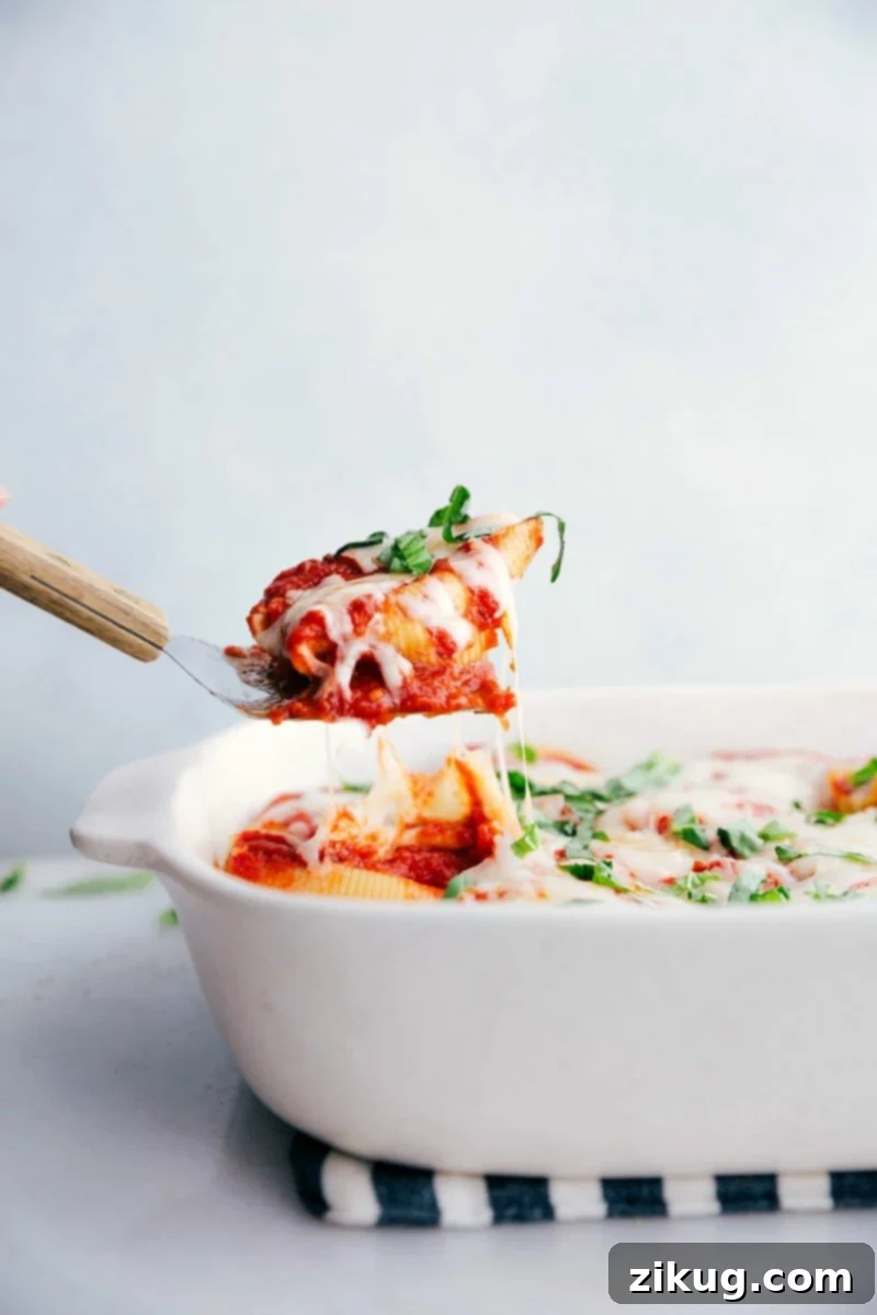 Spatula pulling up a stuffed shell from the pan, showcasing melted cheese and rich marinara sauce with herbs.