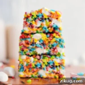 Fruity Pebbles Rice Krispies Treats stacked on top of each other showing the gooey desserts.