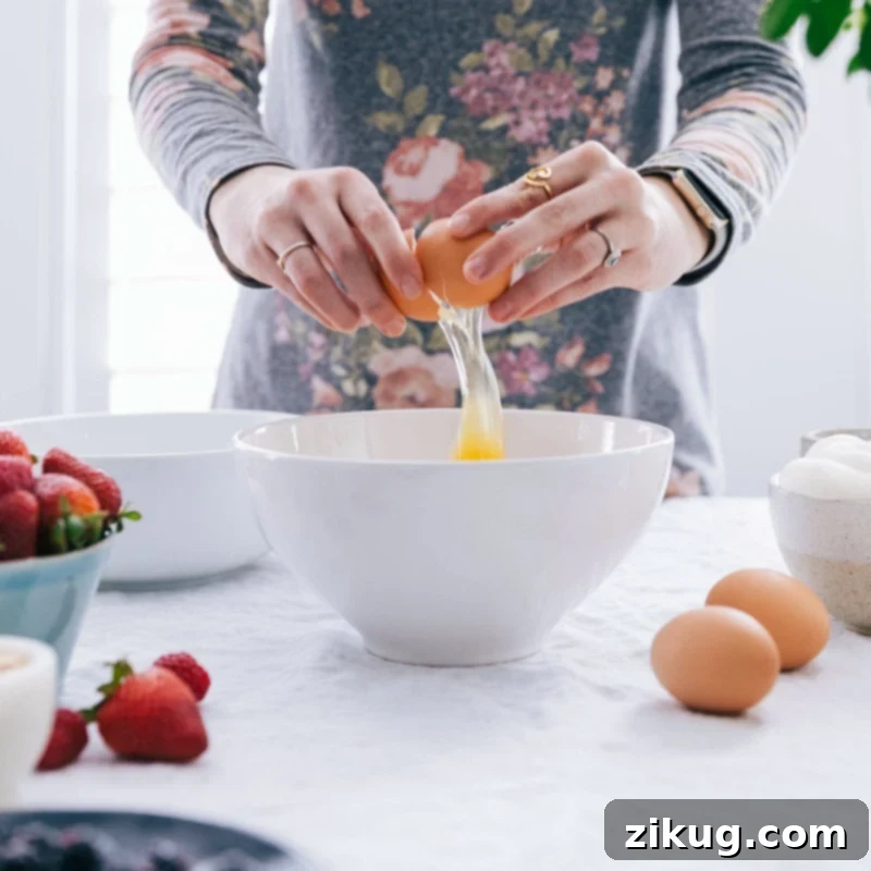 Essential Ingredients for the Best Waffle Recipe! An egg being cracked into a mixing bowl, illustrating the start of the waffle batter preparation.