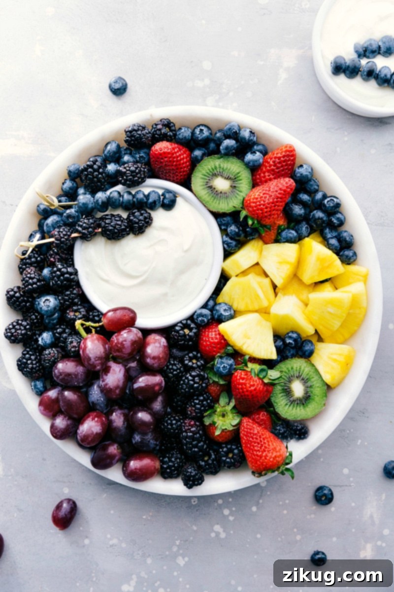 Only four ingredients go into this creamy, dreamy Fruit Dip! It's the perfect smooth, tangy, sweet accompaniment for fresh fruit! Recipe via chelseasmessyapron #withcreamcheese #withmarshmallowfluff #easy #recipe #fruitdip #dip #fruit #summer Image of the ready-to-eat Fruit Dip with a variety of fresh fruits like strawberries, grapes, and pineapple arranged beautifully around it on a serving platter.