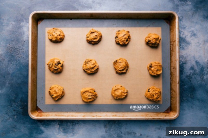 Scoops of cake mix pumpkin cookie dough expertly portioned and arranged on a parchment-lined baking sheet, ready to go into the oven.