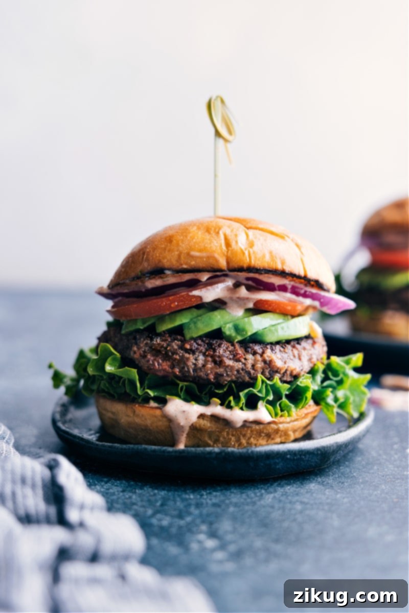 A vibrant and appetizing black bean burger served on a plate, generously topped with an assortment of fresh, colorful vegetables and a rich, flavorful sauce drizzled over the patty and bun.