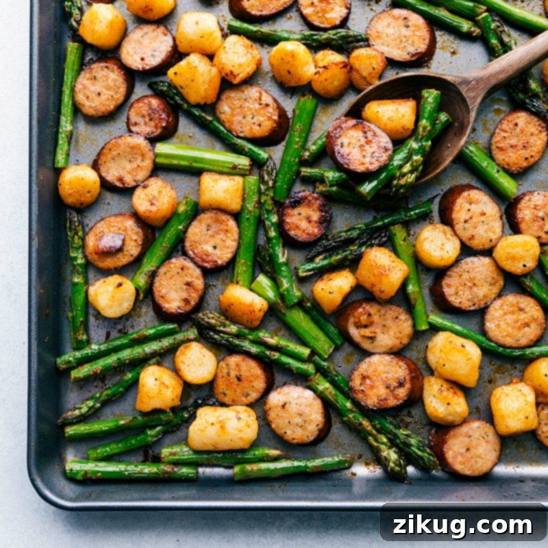 One pan and only EIGHT amazing ingredients make this flavor-packed and nutritious Sausage Pesto and Veggies! Process shot of meal: sausage, asparagus, and gnocchi roasting together on a single sheet pan, showing beautiful browning and tenderization of all ingredients.