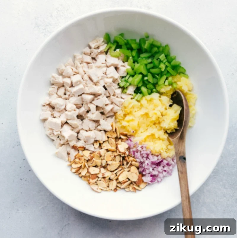 Chicken and Pineapple Ready to Mix A beautiful array of raw ingredients for Pineapple Chicken Salad, including shredded chicken, vibrant pineapple pieces, sliced celery, and diced red onion, all prepared and ready to be mixed in a large bowl. This image captures the freshness and quality of the components before combining.