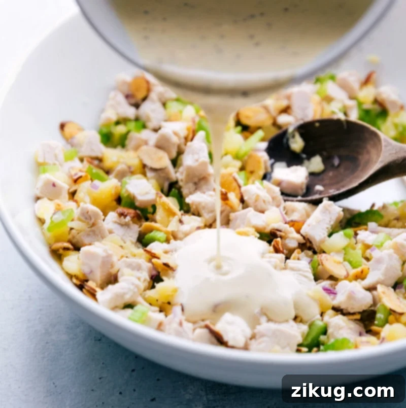 Island Pineapple Chicken Salad 3 The final step: a stream of creamy dressing is being poured over the vibrant Pineapple Chicken Salad, preparing it for the gentle toss that will marry all the sweet, savory, and fresh flavors into one cohesive, delicious meal.