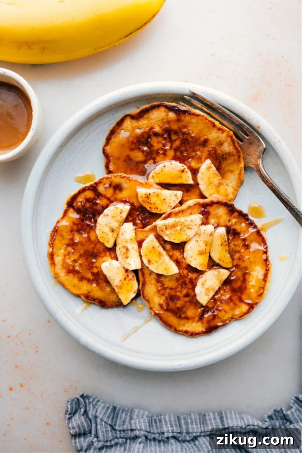 Delicious Warm Banana Pancakes with Fresh Bananas and Syrup Warm banana pancakes stacked high on a plate, garnished with fresh banana slices and generously drizzled with golden maple syrup, creating a mouth-watering breakfast scene.