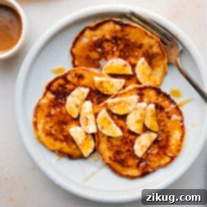 Warm banana pancakes stacked on a plate, topped with fresh banana slices and generously drizzled with syrup, creating a delicious and inviting breakfast.