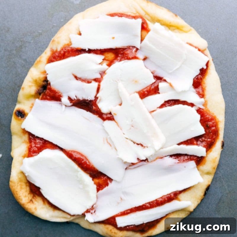 Adding Mozzarella Cheese on Top of Pizza Sauce on Naan Bread Chunks of fresh mozzarella cheese being added on top of the sauce.