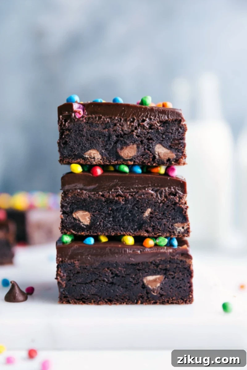 Homemade cosmic brownies stacked, showcasing their delicious layers, fudgy texture, shiny chocolate frosting, and topped with colorful candies - a truly nostalgic and irresistible treat.