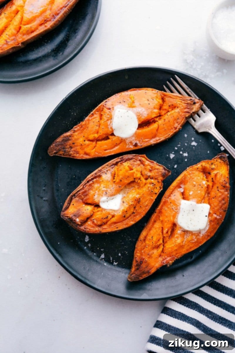 Delicious Baked Sweet Potatoes Recipe Two halves of perfectly baked sweet potatoes on a white plate, glistening with a pat of melting butter and a sprinkle of fresh herbs.