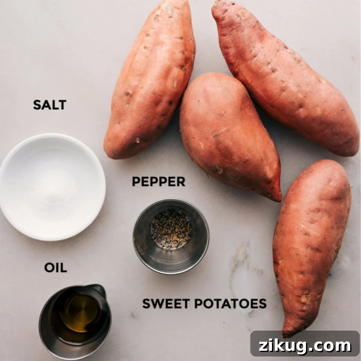 Perfect Baked Sweet Potatoes 2 Four simple ingredients for baked sweet potatoes: fresh, whole sweet potatoes, a bottle of olive oil, a shaker of salt, and a pepper mill, neatly arranged on a kitchen counter.