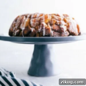Cinnamon roll monkey bread baked and ready to eat, sitting on a cake stand, with icing dripping, delicious and full of flavor.