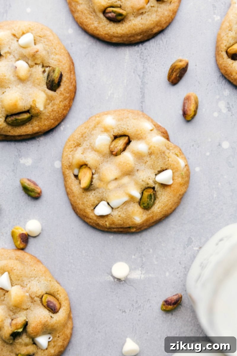 Freshly Baked Pistachio Cookies with White Chocolate Chips A batch of freshly baked pistachio cookies, baked to a golden-brown perfection, filled with flavor, white chocolate chips, and pistachio bits, ready to be savored. Each cookie showcases a beautiful green hue from the pistachios, contrasting with the melted white chocolate.