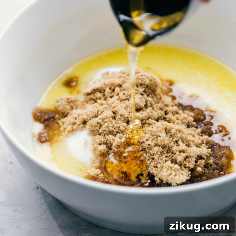 Adding Honey to Wet Ingredients Adding rich, golden honey to a bowl of wet ingredients, showcasing the viscous liquid as it pours in, contributing its natural sweetness and unique flavor to the cookie dough mixture.