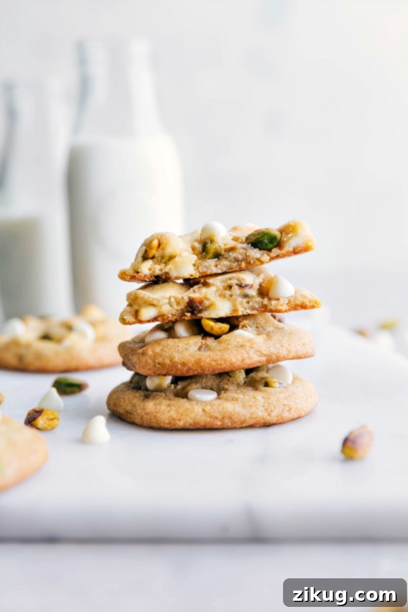 Pistachio Cookies Recipe - Delicious Stacked Cookies The finished pistachio cookies recipe, with cookies perfectly stacked on top of each other and one cookie carefully broken open to reveal its delightful chewy texture, melted white chocolate chips, and vibrant pistachio bits. This new favorite cookie is ready to be enjoyed.