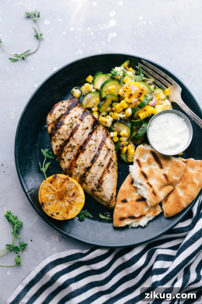 Authentic Greek Chicken with Zucchini and Corn Salad A beautifully plated Greek chicken dinner, featuring succulent grilled chicken alongside a fresh zucchini and corn salad, served with warm naan bread and creamy tzatziki sauce. This vibrant meal is both delicious and visually appealing, promising a taste of the Mediterranean.