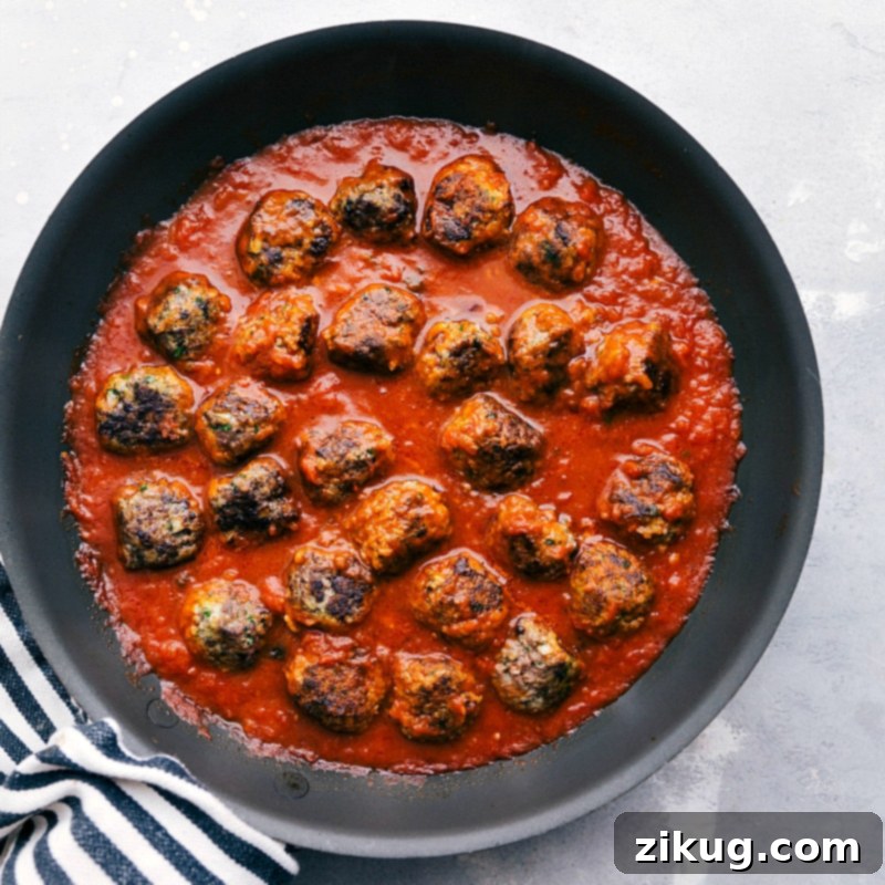 The Best Homemade Meatball Sub Recipe 3 Meatballs gently simmering in marinara sauce, a crucial step in the preparation of the meatball sub recipe, ensuring the infusion of rich flavors.