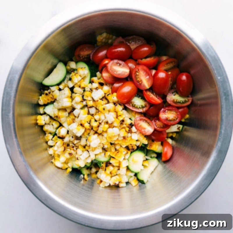 A bowl filled with the corn and zucchini salad, the addition of fresh tomatoes and more ingredients, capturing the moment before mixing to create a flavorful salad.