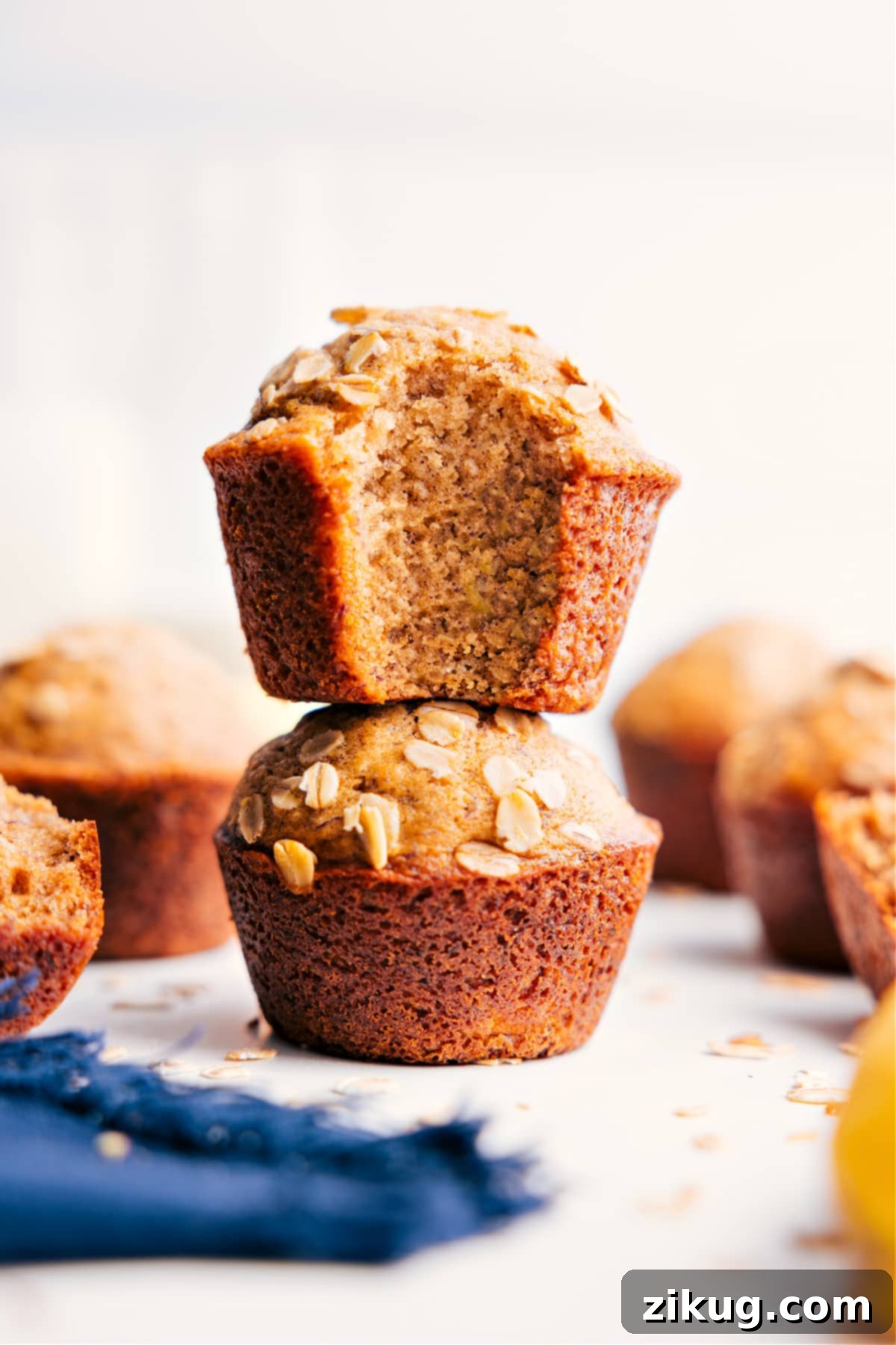 The Best Healthy Banana Muffins Recipe Healthy Banana Muffins stacked with a bite taken out of the top one, revealing the moist and delicious interior, garnished with a few whole oats.