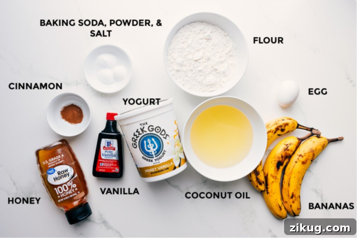 Ingredients In Healthy Banana Muffins All the ingredients prepped for easy assembly, including flour, eggs, fruit, coconut oil, yogurt, baking soda, powder, salt, cinnamon, vanilla, and honey, laid out on a light surface.