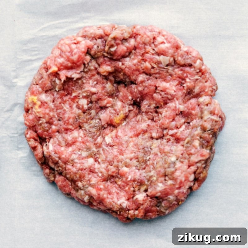 Shaping the Raw Patty for Teriyaki Burger - Demonstrating Meat Shaping Technique A raw burger patty being skillfully shaped on parchment paper, demonstrating the technique for firm and even patties.