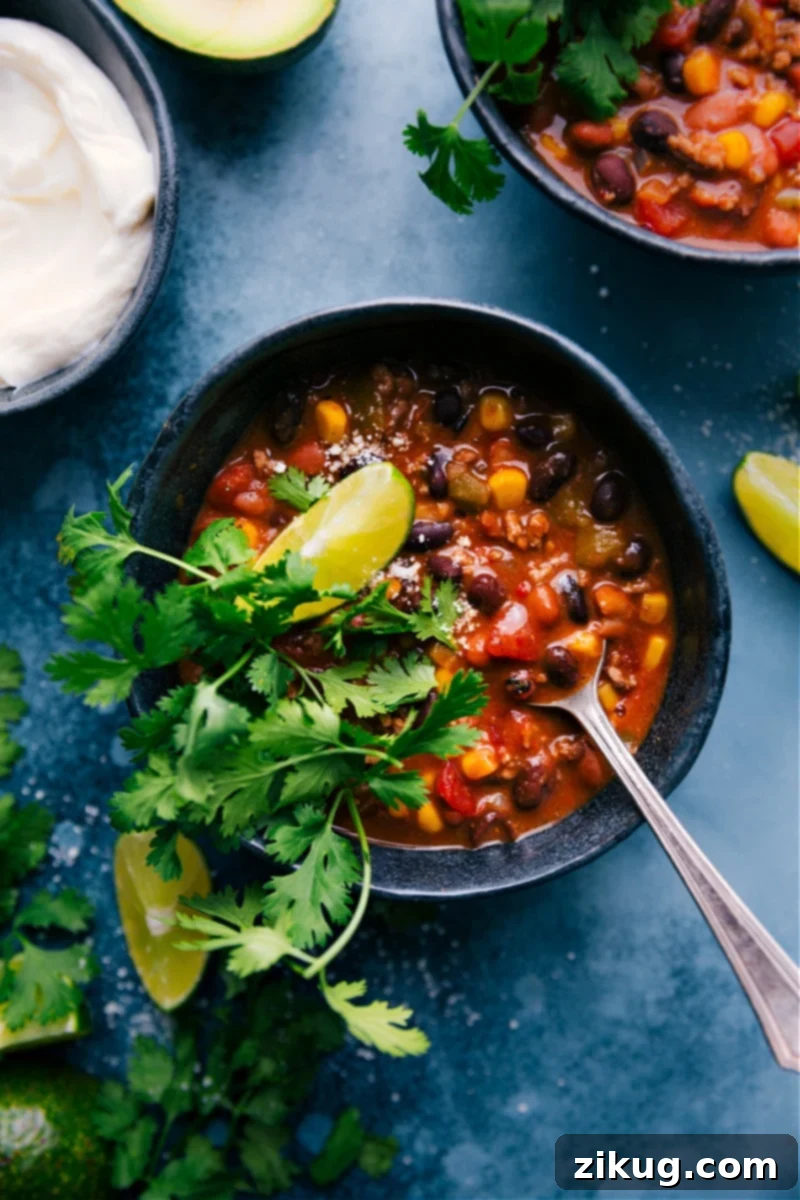 Delicious and Easy Taco Chili: A Family Favorite for Dinner Tonight! Overhead image of a vibrant bowl of Taco Chili, garnished with generous amounts of shredded cheese, a dollop of sour cream, and fresh cilantro, suggesting a delicious and hearty meal perfect for any occasion.