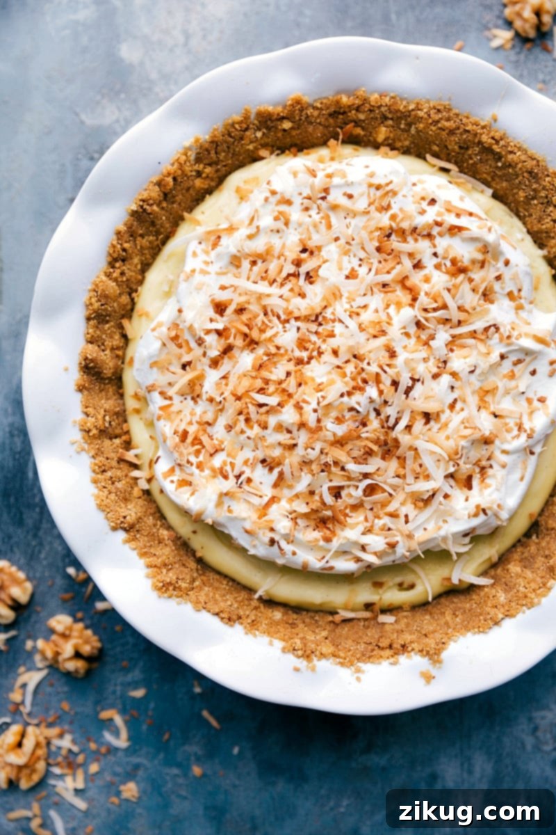 Incredible and rich Coconut Cream Pie with a walnut graham cracker crust, fresh homemade whipped cream, and toasted coconut to top it off. Overhead image of a beautifully prepared Coconut Cream Pie, with a slice removed, ready to be served.