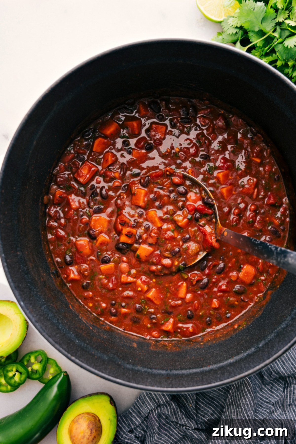 The Best Sweet Potato Chili Recipe A big scoop of Sweet Potato Chili coming out of the pot, rich with vegetables and beans.