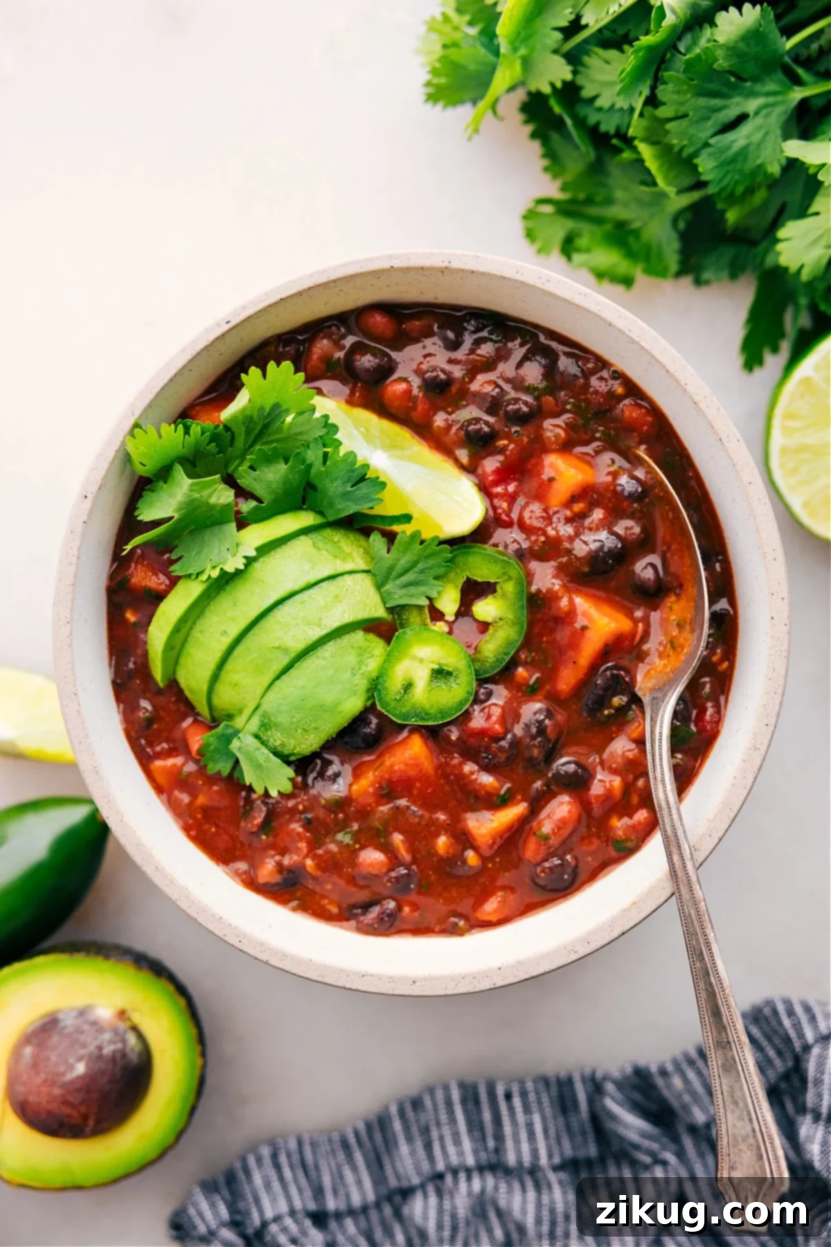 Sweet Potato Chili With All The Toppings A bowl of Sweet Potato Chili elegantly topped with fresh cilantro, vibrant jalapeño slices, a zesty lime wedge, and creamy avocado, ready to be enjoyed.