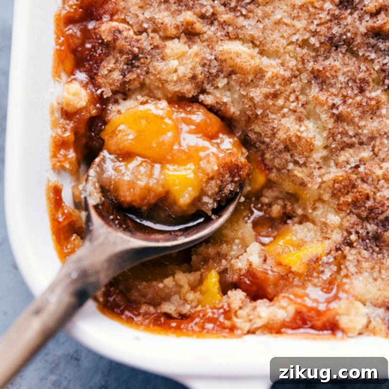 A spoonful of the dessert being scooped out of the casserole dish, revealing the delicious fruity interior.