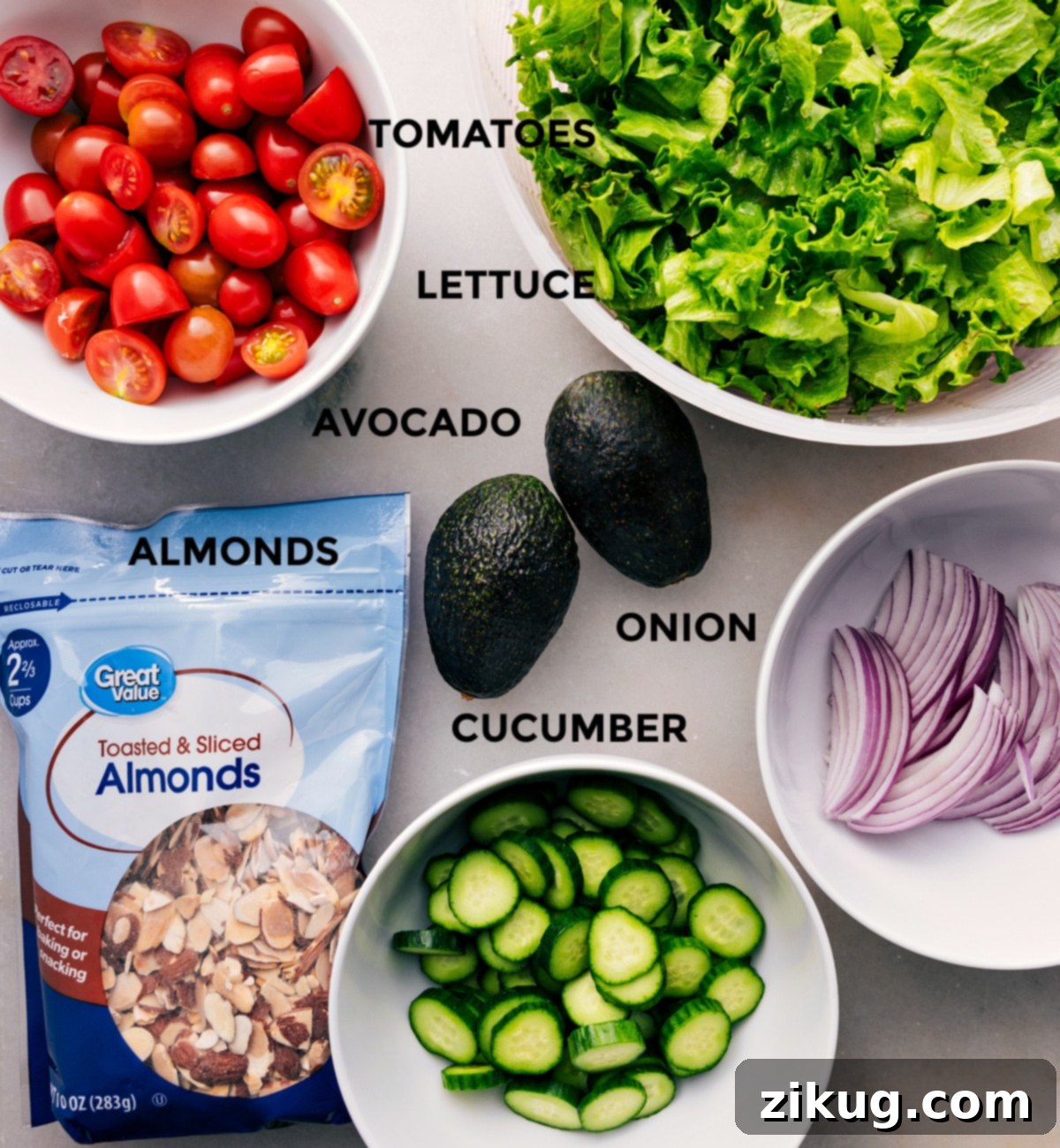 Fresh, vibrant ingredients for Crispy Chicken Salad are prepped and arranged: crisp romaine, halved cherry tomatoes, sliced avocado, red onion, cucumber, and roasted almonds.