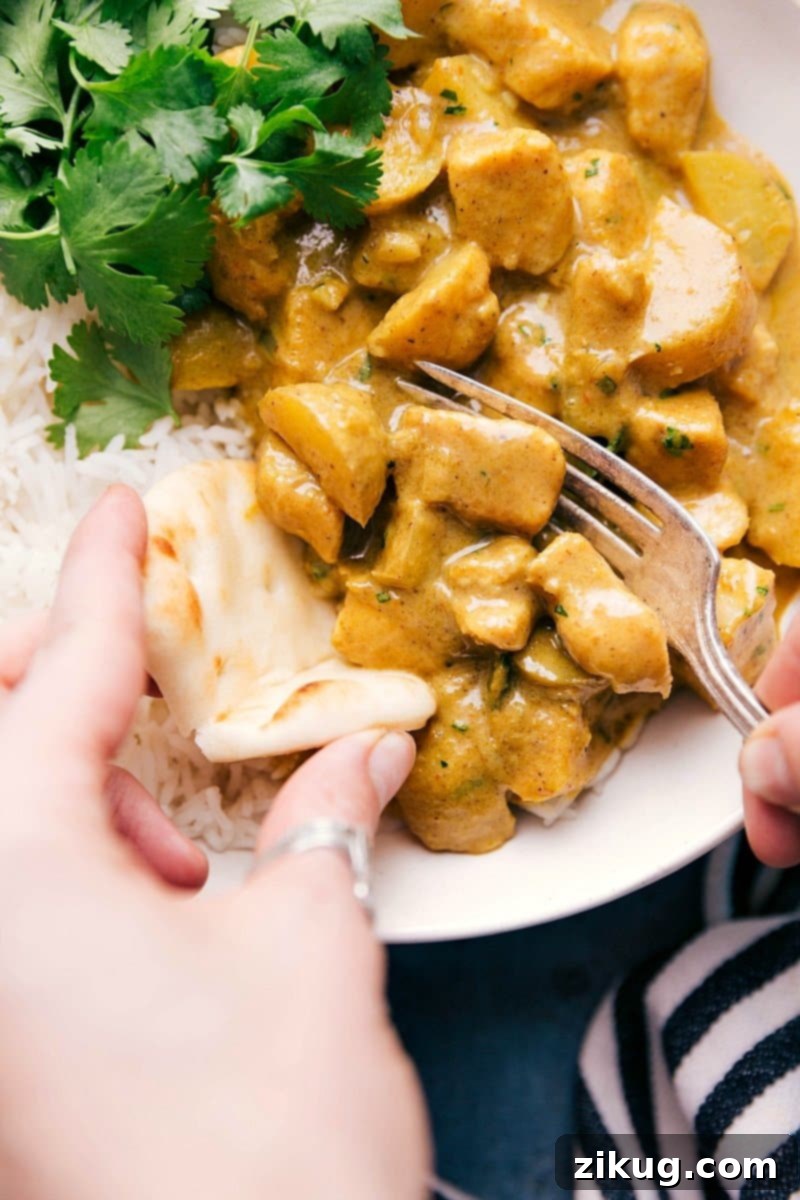 A generous serving of vibrant Yellow Chicken Curry with tender chicken and potatoes, presented beautifully over fluffy white basmati rice and a piece of golden naan bread ready for dipping.