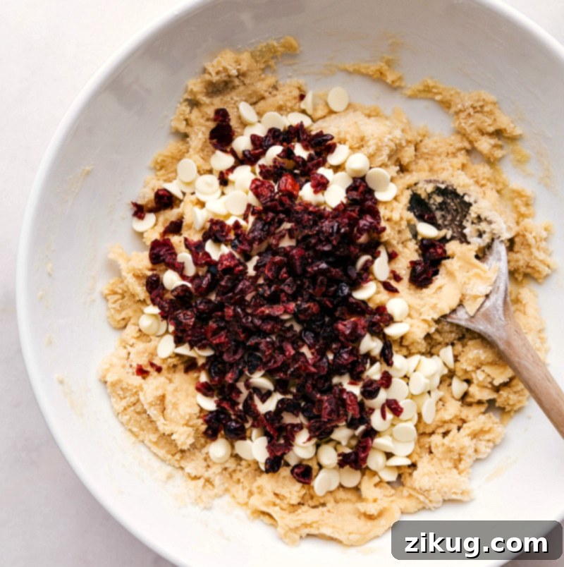 Crafting Flavorful Cookies: Mixing White Chocolate and Cranberries for a Complementary Taste Vibrant white chocolate chips and jewel-toned cranberries being gently folded into rich, creamy cookie dough, promising a burst of complementary flavors and textures in every bite.