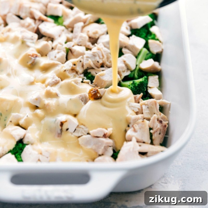 Pouring creamy, cheesy sauce over the layered broccoli and chicken in the casserole dish.