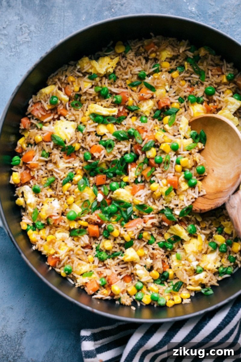 Plate of flavorful fried rice with a mix of vegetables, egg, and seasonings, garnished with green onions.