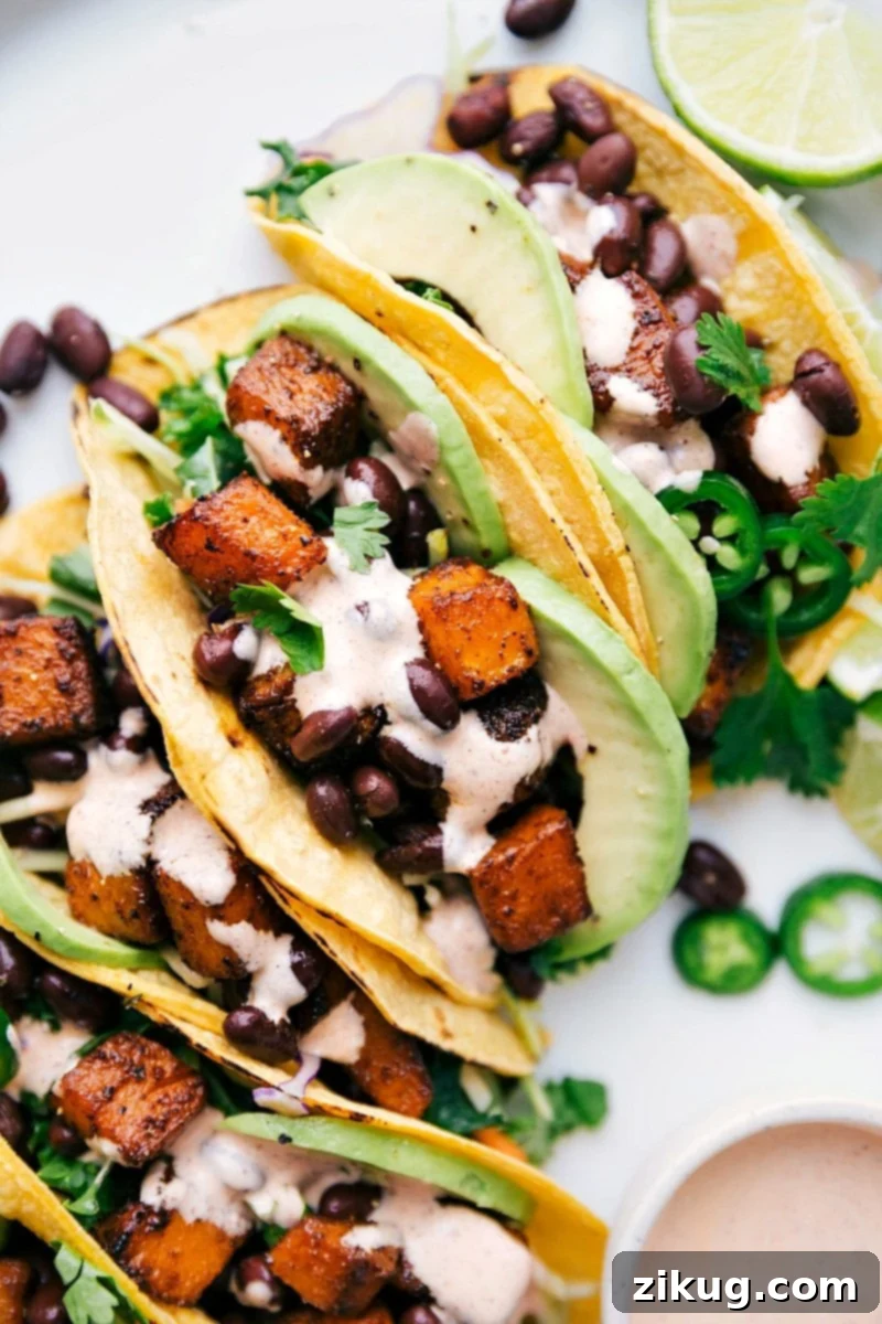 Overhead image of beautifully plated Butternut Squash Tacos with fresh lime wedges, avocado slices, and cilantro, served with the creamy sauce on the side.