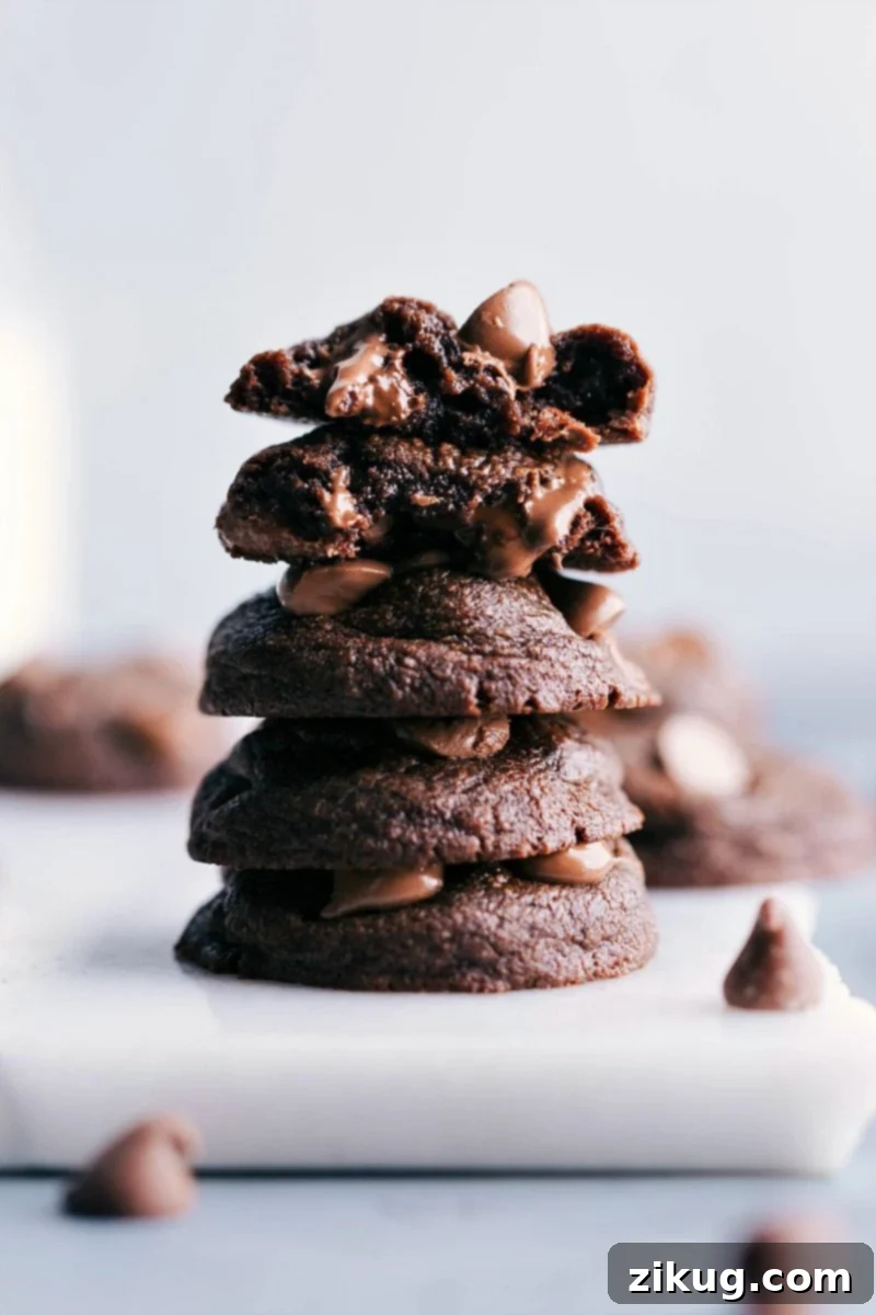 Deliciously Decadent Fudge Brownie Cookies, One Split Open Stacked fudge brownie cookies with one split in half to reveal their rich and gooey inside.