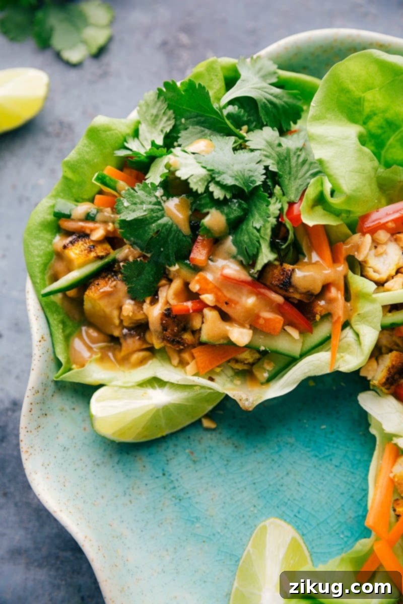 Plate of vibrant peanut chicken lettuce wraps, showcasing crisp green lettuce cups overflowing with savory chicken, colorful vegetables, and a generous drizzle of rich peanut sauce, garnished with fresh cilantro and crushed peanuts.
