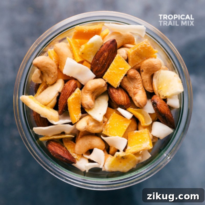 A delicious and healthy tropical trail mix, brimming with nuts, dried fruits, and coconut, beautifully showcased in a clear glass jar.
